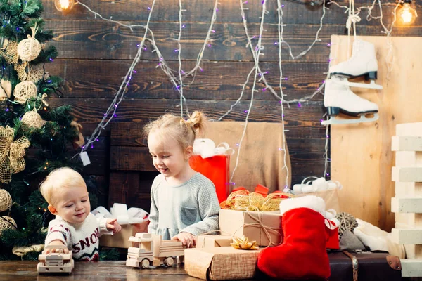 Kışın giyinmiş küçük mutlu çocuk Noel ağacının yanında Noel Baba 'yı düşün. Gülümseyen çocuk Noel ağacının arkasından dikizliyor. Ahşap arka planda Noel hediyesi olan mutlu çocuk.. — Stok fotoğraf