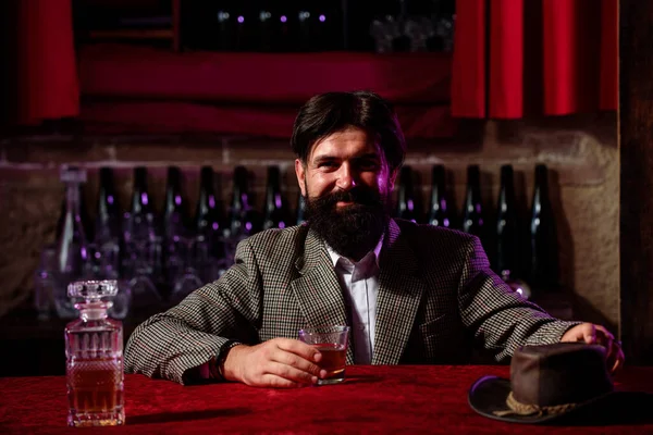 Homem trabalhador vintage com barba comprida segurando uísque. Sentado no bar. — Fotografia de Stock