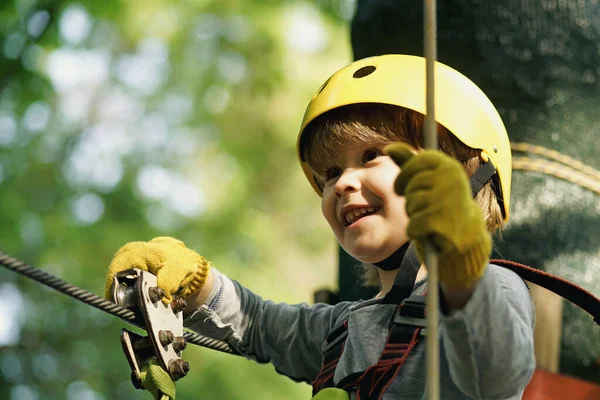 Climber child on training. Cute little boy in climbing safety equipment in a tree house or in a rope park climbs the rope. Safe Climbing extreme sport with helmet — Stock Photo, Image