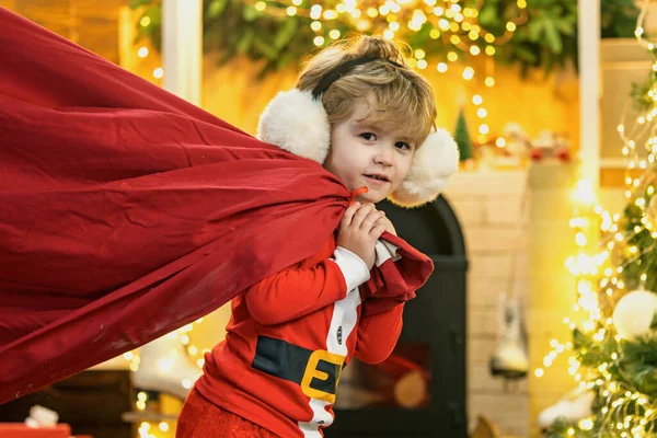 Filha do Pai Natal. Santa ajudante segurando um saco vermelho com presentes. Feliz Natal e feliz ano novo. Surpreendido Little Santa na sala de Natal. — Fotografia de Stock