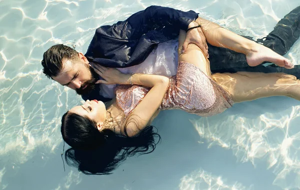 Ett ungt par kramar i poolen. Våta aftonklänningar. Mörhet i klart vatten. Reklam och kommersiell design. En skäggig man i jacka och en flicka i klänning föll i vattnet.. — Stockfoto