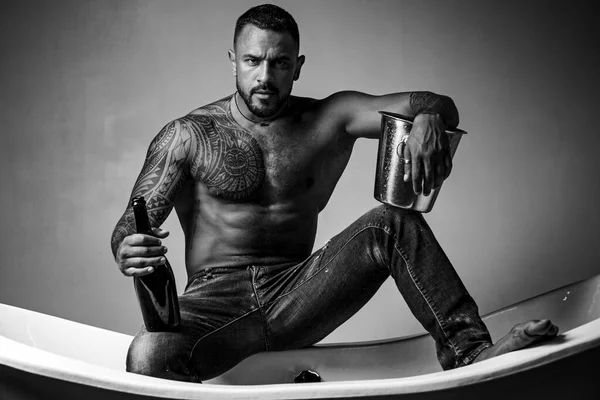 Celebração do champanhe. Homem bonito com corpo tatuado em fundo cinzento. Festa noturna sexy - jovens amantes. Moda homens pernas em jeans. — Fotografia de Stock