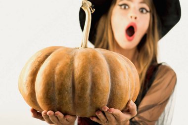 Komik surat ve şaşırmış kadın. Balkabağıyla poz veren kadın. Cadıların şapkası ve kostümü içinde balkabağı tutan genç ve güzel bir kadın..