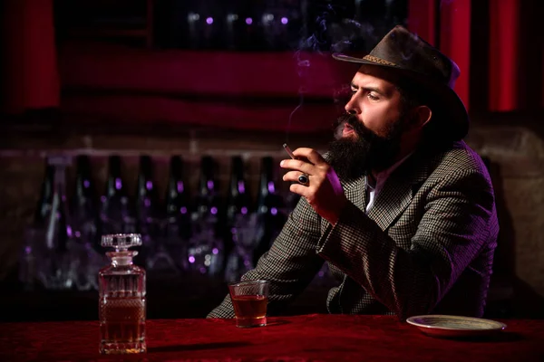 Homem hipster barbudo fumando cigarros com copo de wiskey. — Fotografia de Stock