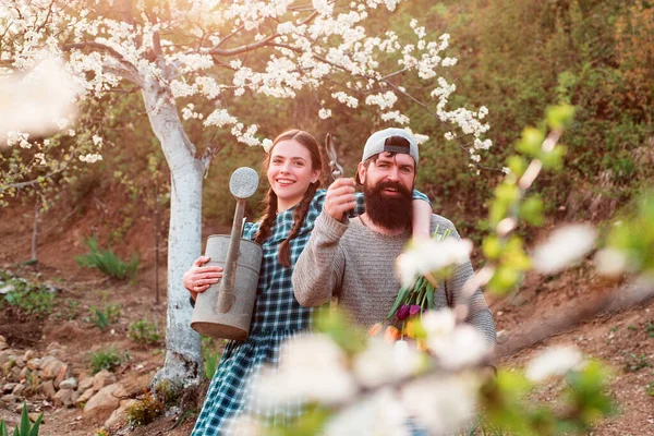 Lustiges Gärtnerehepaar mit Gartengeräten im Frühlingshintergrund. Frühlingspaar verliebt. — Stockfoto