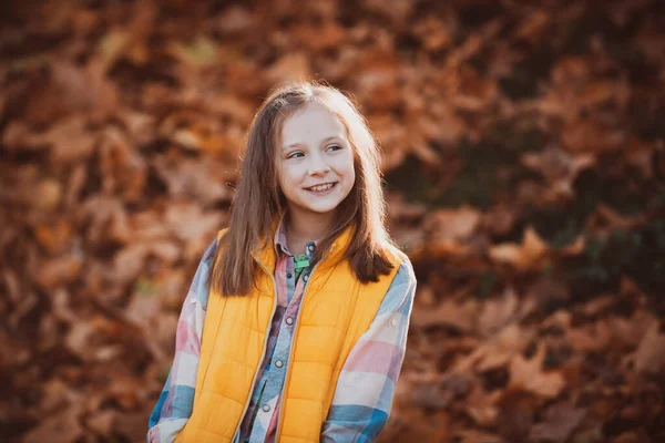 Glückliches Kind auf einem Hintergrund von Herbstbäumen. Posieren im herbstlichen Park. Entzückend glückliches Mädchen, das im Herbstpark mit fallenden Blättern spielt. Liebenswertes Mädchenporträt an einem schönen Herbsttag. — Stockfoto