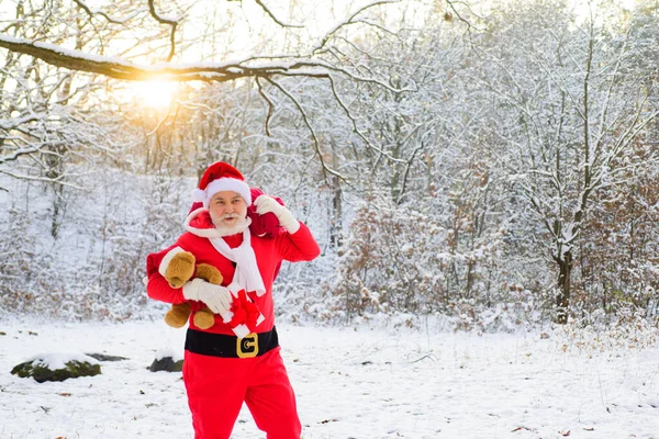 Santa Claus en Nochebuena lleva regalos a los niños en una bolsa en el paisaje de nieve. —  Fotos de Stock