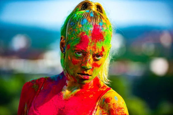 Färg ansikte med färgglada holi stänk. Närbild porträtt av en ung kvinna med färgglada holi pulver. Flerfärgat ansikte helt täckt med ljus holi färg. — Stockfoto