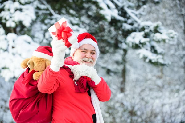 冬のフィールドでハッピーサンタ。クリスマスの夜に面白いサンタクロースは袋に子供たちにプレゼントを運んでいます. — ストック写真