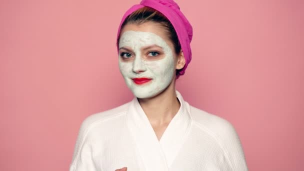 Chica con una máscara en la cara arrojar una manzana sobre un fondo rosa. Hermosa chica con máscara cosmética en su cara. Concepto de belleza facial. Tratamiento facial femenino. — Vídeos de Stock