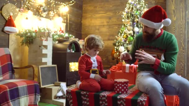 Vater und Sohn bereiten sich beim Weihnachtszauber vor. Vater und Kind öffnen Weihnachtsgeschenke. Kind mit Eltern in Weihnachtsmütze genießt Neujahr. — Stockvideo