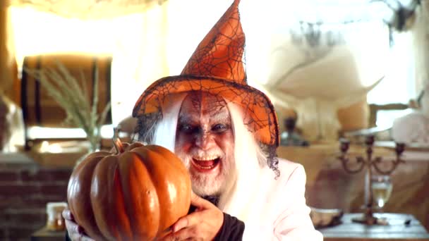 Il vecchio e 'pronto per la festa di Halloween. Il mago malvagio tiene la zucca arancione. Un mago maturo col cappello da strega. Halloween mistico, luce magica e stregoneria con incantesimo e incantesimo. — Video Stock