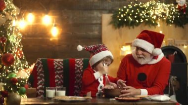 Komik Noel Baba ve şirin çocuk geleneksel Noel tatlıları pişiriyor. Evde tatil pastanesi. Mutlu yıllar çocuklar..