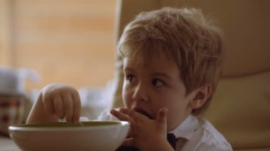 Küçük çocuk yulaf lapasının tadını çıkarıyor. Komik çocuk sütlü yulaf lapası yiyor. Çocuk çizgi film izliyor.