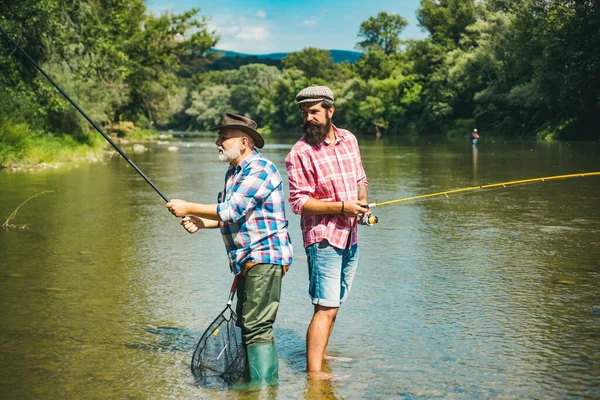 Amici uomini con canna da pesca e rete. Impostare asta con gancio linea platina. La leggenda si è ritirata. Due amici maschi vestiti di camicie da pesca insieme a rete e canna durante la luce del mattino sul lago. — Foto Stock