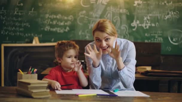 Jolie enseignante et enfant d'âge préscolaire souriant à la caméra à l'arrière de la salle de classe à l'école primaire. — Video
