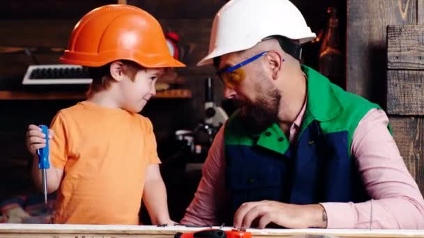 Kinderen leren gereedschap gebruiken met papa. Ouder in beschermende helm leren kleine zoon om verschillende gereedschappen te gebruiken in de school workshop. Vaderschap concept. Vader en zoon werken samen. — Stockvideo