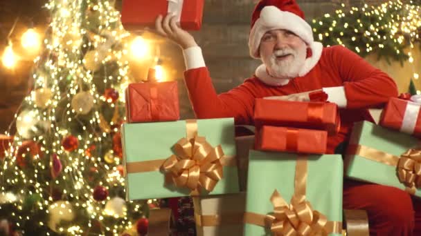 Caixas de presentes e feliz ajudante santas. Dia de Acção de Graças e Natal. Papai Noel perto da lareira e árvore de Natal com presentes. — Vídeo de Stock