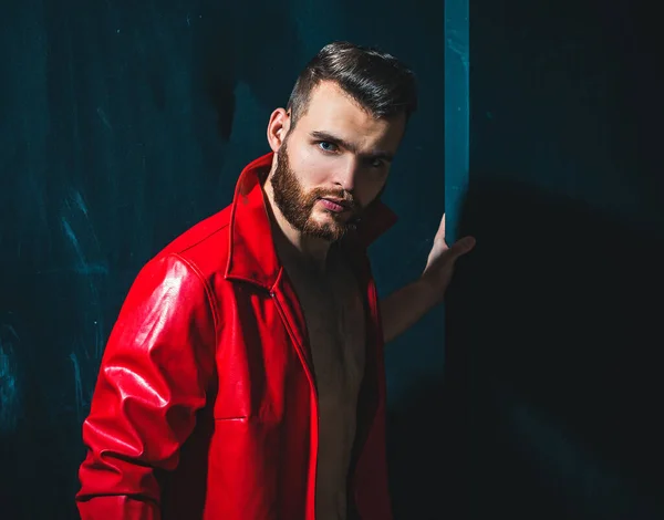 Portret młodego przystojniaka. Przystojny mężczyzna w czerwonej skórzanej kurtce na nagim muskularnym tułowiu na ciemnym tle, patrzący na kamerę. — Zdjęcie stockowe