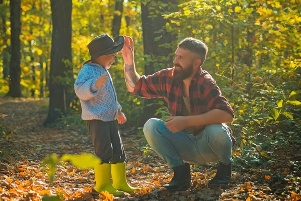 Батько і син грають у осінньому лісі. Маленький хлопчик з батьком розмовляє восени на відкритому повітрі. Стильний чоловік з сином, тато з молодим блондинкою в осінньому парку . — стокове фото