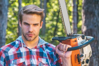 Oduncu işçi ormanda elektrikli testereyle dikiliyor. Elektrikli testere. Oduncu gibi poz veren şık bir genç adam. Bıçkıhanede elektrikli testereli bir oduncu. Kereste hasadı.