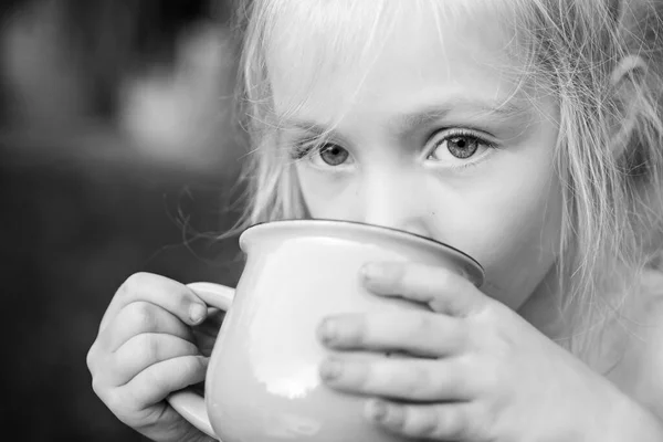 Een mok in handen van een kind. Meisje drinkt iets. Buiten kind in de natuur. — Stockfoto