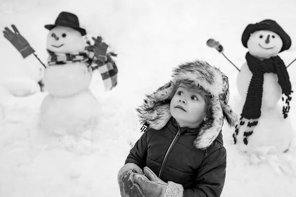 스노 먼과 웃긴 아이는 친구가 붉은 코를 가진 채 겨울 모자와 스카프를 쓰고 서 있습니다. 메리 크리스마스, 해피 뉴이어. 크리스마스 겨울 아이들. — 스톡 사진