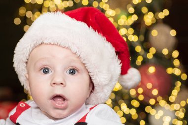 Komik bir çocuk yüzü, yakın plan. Noel Baba kıyafetleri içinde bebek portresi ve Noel şapkası.