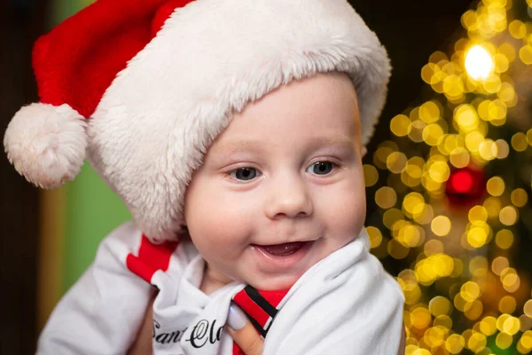 快乐微笑的孩子面对特写。在圣诞树附近戴着圣诞礼帽的可爱的婴儿脸。快乐童年，1岁的孩子。新年孩子们. — 图库照片