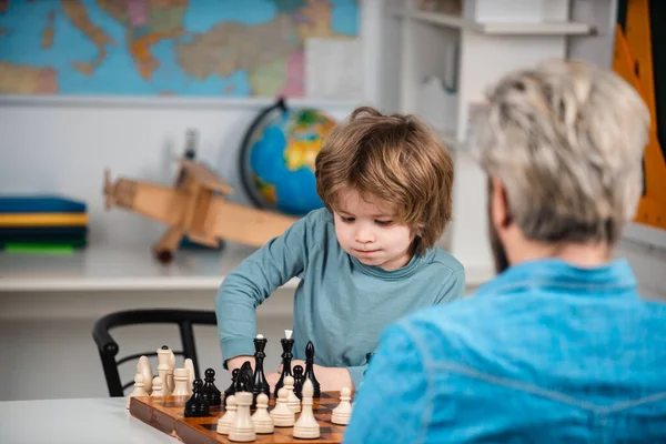 Petit garçon concentré - père et fils assis à la table et jouant aux échecs. Professeur et écolier jouant aux échecs en classe. — Photo