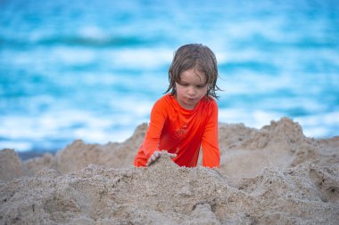 Çocuklarla tatile. Çocuk kumsalda eğleniyor. Çocuk denizde kumdan kale yapıyor..