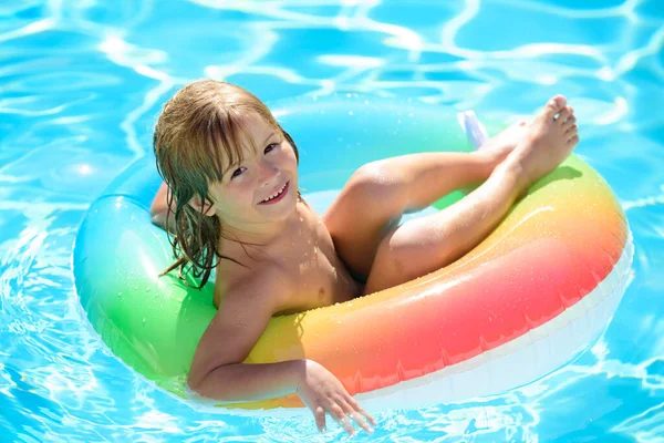 Kinderen zitten op een opblaasbare ring in het zwembad. Zomervakantie plezier. klein kind spelen in blauw water met drijvende ring. — Stockfoto