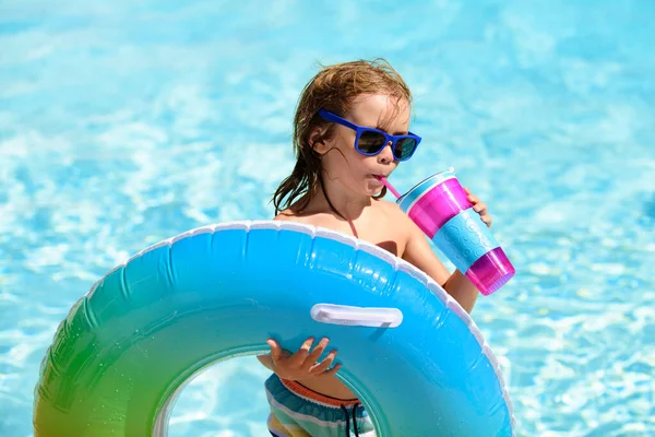 Kid in sunglasses and summer cocktail relaxing with toy ring floating in a swimming pool. — Stock Photo, Image