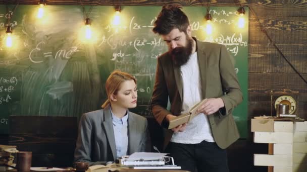 Une femme écrivain blonde et professeur barbu tient un livre contre un tableau en classe. Journaliste rétro. — Video