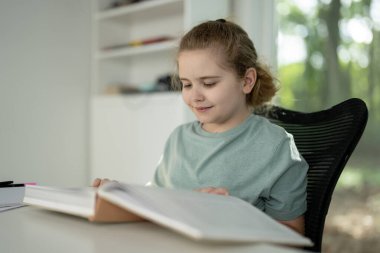 Çocuk rahat odada kitaptan zevk alıyor. Gülümseyen büyük bir kitap okuyan çocuk. Akıllı öğrenci açık bir kitap tutuyor. Evde kitap okuyan sevimli bir çocuk. Çocuk kitaplardan bilgi öğreniyor.