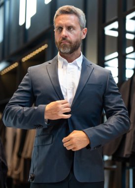 Takım elbiseli, takım elbiseli bir adam. Bir iş adamı mağazada şık bir takım elbise seçer. Modayı takip eden bir müşteri resmi kıyafet alırken ceketi inceler. Klasik kıyafetli çekici bir manken.