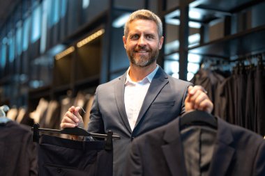 İş adamı için uygun. İyi giyimli bir erkek model bir butikte poz veriyor. Perakende satış elemanı şık bir adamın mükemmel takımı bulmasına yardım eder. Bir mağaza müdürü şık bir takım elbise ayarlar.