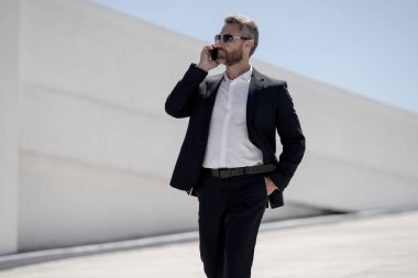 Ofis çalışanı dışarıda cep telefonuyla konuşuyor. Girişimci cep telefonundan konuşur. Yönetici telefon görüşmesi yapıyor. Telefon kullanan şık bir iş adamı. İş görüşmesi. Meşgul iş adamı telefonda konuşuyor.