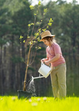 Bahçede küreği olan bir çocuk. Çocuk dikme ağacı. Sulama kabı olan küçük bir bahçıvan. Çocuklarla bahar bahçesi