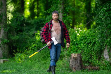 Ekose gömlekli oduncu ve kot pantolonlu. Yaz tahtasında büyük bir balta taşıyor. El işi. Doğal ortam. Ormanda baltası olan oduncu. Çalışkan adam. Baltası ya da baltası olan kaba sakallı bir adam.