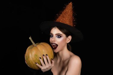 Cadı şapkalı, siyah stüdyodaki cadılar bayramı kadını. Cadılar Bayramı kızı balkabağı portresi tutuyor. Cadılar Bayramı kostümlü kadın model. Cadılar Bayramı kadın portresi büyücülük tarzıyla