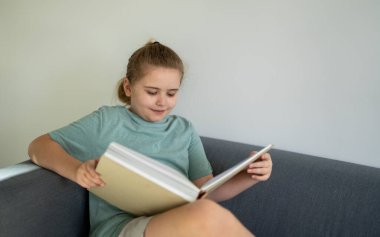 Çocuk rahat bir odada kitap okuyor. Gülümseyen büyük bir kitap okuyan çocuk. Zeki öğrenci kitap okuyor. Evde ders çalışıp kitap okuyan sevimli bir çocuk. Çocuk kitaplardan öğreniyor.