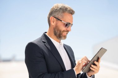Açık havada tablet kullanan mutlu bir iş adamı. Tabletle başarılı bir iş adamı. Dışarıda tablet üzerinde çalışan bir iş adamı. Zarif iş adamı tableti kontrol ediyor. Dijital aygıt kullanan işadamı