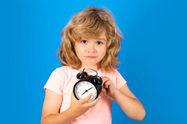 Komik suratlı, çalar saati tutan komik çocuk. Şaşkın çocukla sabah okulu konsepti. Büyük saati ve şok olmuş ifadesi olan bir çocuğun portresi. Çocuk şaşkın bakarken alarm çalıyor.