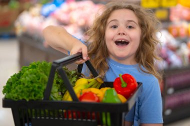 Süpermarkette alışveriş arabası olan bir çocuk. Çocuk taze sebze seçiyor. Yakışıklı çocuk sağlıklı yiyecek için alışveriş yapıyor. Süpermarketteki çocuk. Süpermarketteki çocuk. Çocuk süpermarketten sebze alıyor.