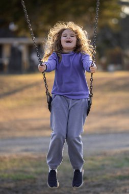 Bahar parkında sallanan neşeli çocuk. Sarı saçlı küçük bir çocuk salıncakta sallanıyor. Parkta gülümseyen mutlu çocuk. Mutlu çocukluk anları. Çocuk dışarıda oynuyor. Çocuk salıncakta eğleniyor. Çocuklar için açık hava oyunu