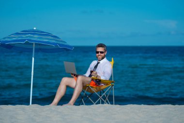 İş tatili. Yaz tatilinde yakışıklı bir iş adamı. İş adamı elinde dizüstü bilgisayarla deniz sahilinde dinleniyor. Yaz işi. Yaz Denizi Sahili 'nde serbest yazar. Yaz haftasonu ve uzak bağımsız çalışma
