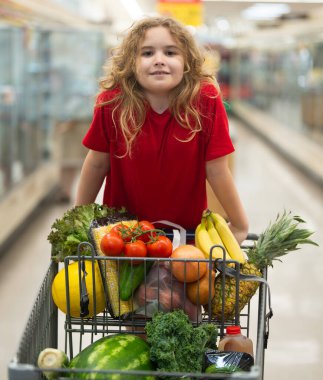 Sepetli çocuk sebze reyonunda. Çocuk markette meyve topluyor. Alışveriş arabalı çocuk. Çocuk süpermarkette alışveriş yapıyor. Çocuk sağlıklı ürünler alıyor. Marketteki çocuk.