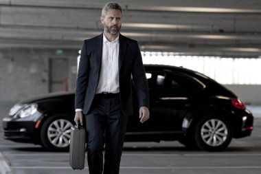 Olgun bir iş adamı. Lüks bir arabanın yanında duran zengin bir işadamı. Küresel. Başarılı bir iş. Zarif bir iş adamı pahalı bir arabanın önünde duruyor. Başarılı iş adamı