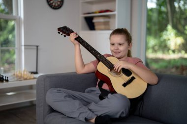 Akustik gitar çalan bir genç. Çocuk oturma odasında gitar çalışıyor. Genç gitarist içeride müzik öğreniyor. Müzik dersi sırasında gitar çalan bir çocuk. Çocuk odada gitar çalıyor.